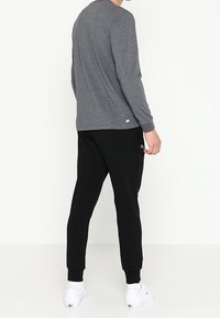 Camiseta gris de manga larga y pantalones de chándal negros, ambos de mezcla de algodón. La camiseta tiene un escote redondo; los pantalones tienen bolsillos laterales y puños ajustados.