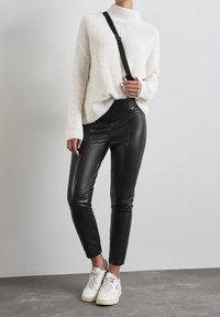 Vit, texturerad tröja med hög krage, kombinerad med svarta läderbyxor med en åtsittande design och sidogårdar, kompletterad med vita sneakers.