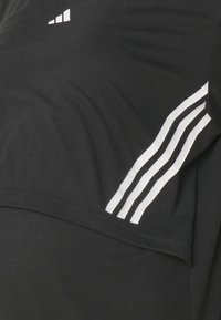 Zwart sportshirt met een wit logo en drie witte strepen langs de mouw. Zacht, glad materiaal met een ontspannen pasvorm.