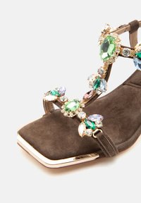 Sandale en daim marron à bout carré, décorée de pierres précieuses multicolores et d'accents métalliques dorés sur les lanières.