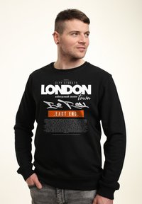 Felpa nera con testo audace bianco e arancione che recita "LONDON" e "EAST END". Realizzata in tessuto morbido con un classico design a girocollo.