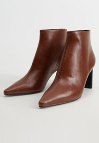 Bottes courtes en cuir marron avec un bout pointu, un design élégant et un talon bloc haut. Présentent un détail de couture minimaliste.