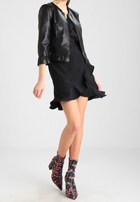 Giacca bomber in pelle nera con orlo arricciato, abbinata a un vestito nero con un design arricciato e stivali alla caviglia a fiori multicolori.