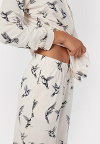 Long-sleeve pajama top and pants in cream, featuring black hummingbird prints. Soft fabric with elastic waistband for comfort.