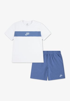 T-shirt blanc Nike avec une bande horizontale bleue et un logo, associée à un short Nike bleu à taille élastique avec le logo sur la jambe gauche.