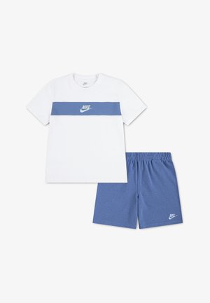 Biele tričko Nike s modrým vodorovným pruhom a logom, v kombinácii s modrými šortkami Nike s elastickým pásom a logom na ľavom stehne.