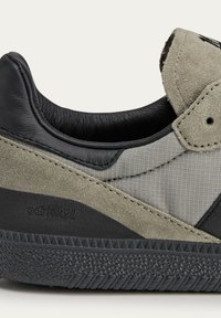 Black leather and gray suede sneaker with a textured rubber sole, featuring stitched accents and a patterned fabric upper.