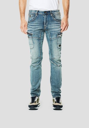 Pantalones vaqueros de mezclilla azul claro con un ajuste slim, con bolsillos cargo, ligero desgaste y costuras en contraste. Combinados con zapatillas negras y beige.