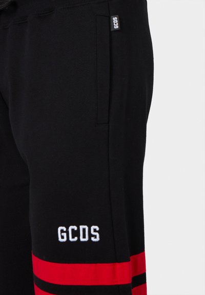 Czarne dresy z czerwonymi i czarnymi paskami oraz białym haftowanym logo "GCDS" po lewej stronie. Zawierają detal kieszeni bocznej.
