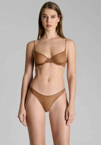 Soutien-gorge beige sans couture et string assorti en tissu léger et transparent. Le soutien-gorge est doté de fines bretelles réglables et d'une couture centrale discrète.