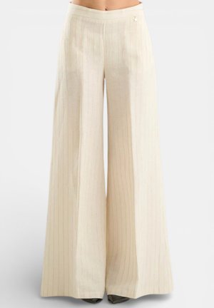 Pantaloni a gamba larga color crema a vita alta con sottili righe verticali, indossati con scarpe nere con punta appuntita.