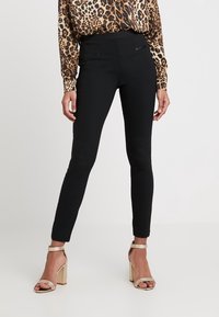 Czarne dopasowane spodnie o gładkiej fakturze i średnim stanie, z kieszeniami z przodu i smukłym krojem, zestawione ze złotymi masywnymi szpilkami.