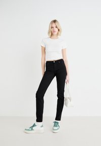 Svarta åtsittande jeans med lätt stretch, kombinerade med en vit kortärmad t-shirt. Vita sneakers med teal-accenter. Liten vit handväska.