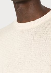 Maglione lavorato a maglia di colore crema chiaro, con scollatura rotonda a coste e un motivo testurizzato sulla superficie. Materiale morbido e traspirante.