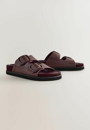 Sandales à glissière en cuir marron avec des sangles à double boucle, une semelle intérieure texturée et une semelle en caoutchouc noire. Présente un design à bout ouvert.