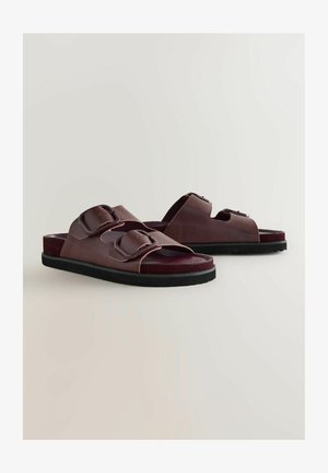 Pruunist nahast libisevad sandaalid, millel on kahekordne tõmblukuga rihm, tekstuuriga jalaplaat ja must kummitald. Omab avatud varba stiili.