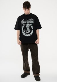Black crew neck oversized t-shirt featuring a graphic print of a cowboy boot and stars with the text "Willie Nelson Outlaw" in white.
