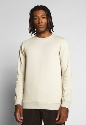 Kremfarget genser i myk tekstil, med lange ermer og rund hals, med ribbestrikkede mansjetter og nederkant. Enkel, minimalistisk design.