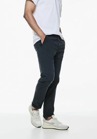 Pantalones chinos azul marino de corte slim, con bolsillos laterales, cintura elástica y dobladillos con puños. Combinados con zapatillas blancas.