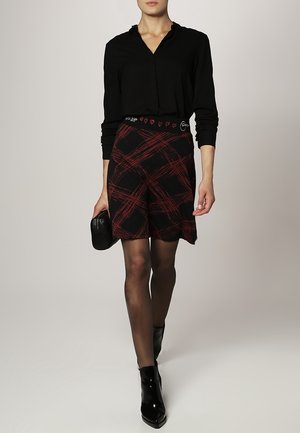 Camisa negra de manga larga con cuello, combinada con una falda de cuadros en rojo y negro y botas hasta el tobillo negras. La falda tiene una cinturilla decorativa.
