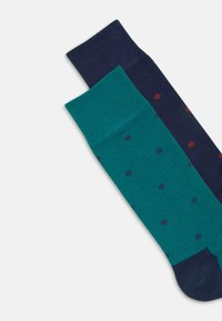 Deux paires de chaussettes montantes ; l'une est unie en bleu marine, l'autre est teal avec des pois navy. Les deux présentent des bords côtelés et des orteils sans couture.
