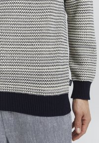 Marineblauer und cremefarbener Strickpullover mit strukturiertem Muster, ausgestattet mit gerippten Bündchen und Saum. Etikett sichtbar an der Seitennaht.