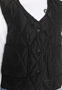 Svart vadderad väst med v-ringning, med fyra framknappar och två stora fickor. Glansigt tyg med en slät yta.
