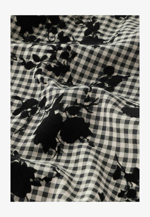 Czarny wzór florystyczny na tkaninie w kratę z małymi kwadratami w czerni i bieli. Faktura wydaje się miękka i nieco teksturowana.