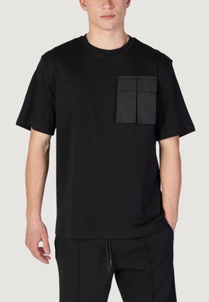 Camiseta de algodón negra de manga corta, con un bolsillo delantero de diseño en dos secciones. Corte simple y relajado con escote redondo.