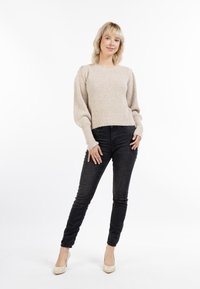 Pulover bej tricotat cu un model texturat, mâneci lungi și un tiv scurt, asortat cu blugi negri mulati și pantofi cu toc bej.