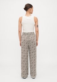 Top alb fără mâneci asociat cu pantaloni evazați, având un model în diamant în tonuri pământii de maro și crem. Textură netedă, talie elastică.