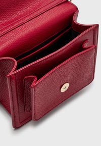 Punainen tekstiilikuosisella nahkalaukku, jossa on läppä suljettuna kultaisella nappikiinnityksellä, sisätiloissa on eri lokeroita ja pehmeä vuori.