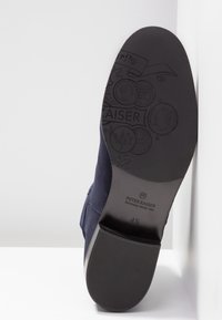 Botte en tissu bleu marine avec une semelle en caoutchouc noire lisse. Les détails en relief remarquables incluent "PETER KAISER" et des motifs semblables à des pièces de monnaie sur la semelle.