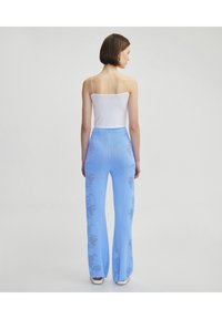 Lichtblauwe flared broek met een bloemenpatroon, gemaakt van een textuurstof. Draag het met een witte spaghetti-strap top.