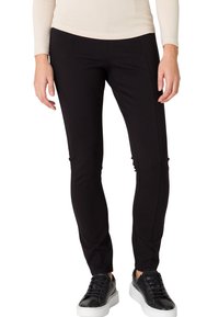 Pantalons noirs ajustés en tissu extensible avec des détails sur les coutures latérales, associés à des baskets noires avec une semelle blanche.