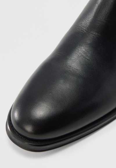 Bota de cuero negro con acabado liso, puntera redondeada y perfil delgado. Presenta un detalle tenue de costura a lo largo del borde de la suela.