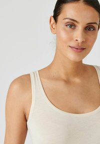 Light beige tank top made of soft fabric, featuring a scoop neckline and wide straps, with seamless edges and minimal stitching details.