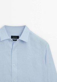 Camicia in lino azzurro chiaro con colletto classico, chiusura frontale con bottoni e texture morbida. Etichetta visibile all'interno del colletto.