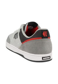 Šedé semišové a textilní tenisky s černým a červeným akcentem, mají gumovou podešev, polstrovaný límec a logo na patě.