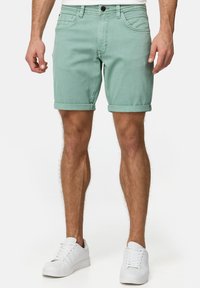 Șorturi din denim verde mentă deschis cu manșete răsucite, design cu cinci buzunare și închidere frontală cu buton. Echipate cu adidași albi.