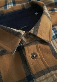 Brun og beige ternet flannel skjorte med knap-down krave og to brune knapper nær halsen, struktureret stof og marineblå inderside.