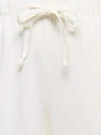 Ceinture élastique blanche avec un cordon en tissu noué sur un tissu doux et texturé, probablement partie d'un pantalon décontracté ou de détente.
