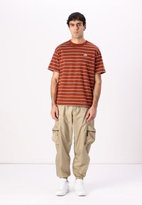 Rød- og hvidstribet bomulds t-shirt med korte ærmer og et lille logo, parret med beige cargo bukser med sidelommer og hvide sneakers.