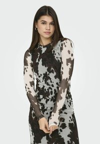 Robe à manches longues dotée d'un motif de vache noir et blanc, avec une silhouette ajustée et un tissu lisse. Poignets accentués.