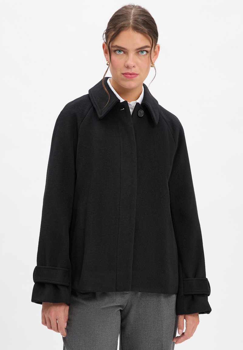 Zwarte wolmix jas met een platte kraag, knoopsluiting en klokvormige mouwen. Soepele textuur en op maat gemaakte design, gestyled met grijze broek.