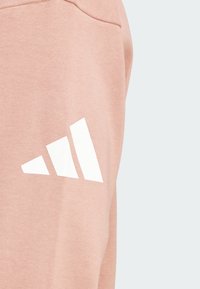 Pantaloni della tuta in cotone rosa con logo a tre strisce bianche sul lato, caratterizzati da una superficie liscia e un taglio moderno.