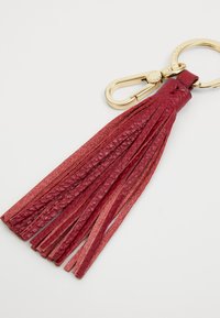 Rød lær tassel nøkkeholder med flere lange tråder, festet til en gullmetallnøklering og -klips. Strukturert overflate og glatte kanter.