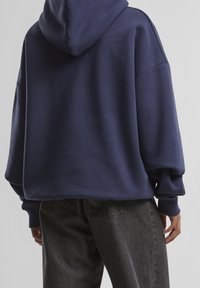 Sweat à capuche oversize bleu marine avec une capuche, des poignets côtelés et des épaules tombantes. Associé à un jean taille haute gris foncé.