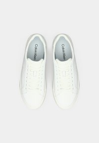 Baskets en cuir blanc avec lacets plats, bout rond, et logo embossé sur le côté. Semelle intérieure douce de couleur bleu clair avec le nom de la marque. Texture lisse sur toute la surface.