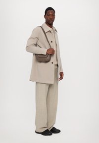 Trench coat bej, bluză tricotată de un bej deschis, pantaloni largi gri deschis și pantofi negri. Geantă mică de umăr maro cu accente de argint.